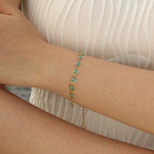 Detail of a gold heart bracelet with teal enamel inlays and adjustable extender chain