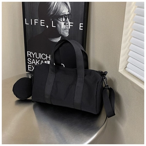 Detail of a minimalist black canvas cylindrical travel bag with a round coin purse charm
