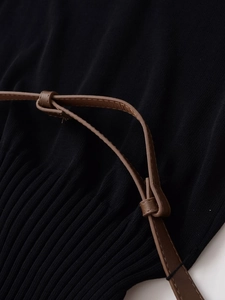 Close-up of black knit fabric texture with pleated details and a slim brown faux leather belt