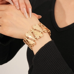 Détail du large bracelet cœur doré avec texture en métal brossé sur un poignet féminin