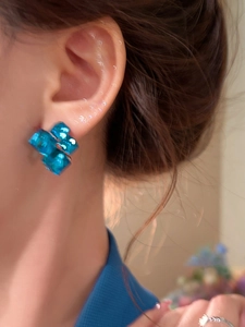 Close-up of elegant blue geometric square stud earrings on model with floral background