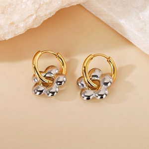 Detail of gold hoops with silver flower charms on neutral stone background