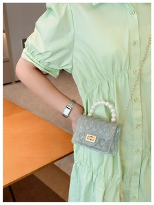 Detail of silver glitter jelly bag with pearl handle and golden chain on green dress