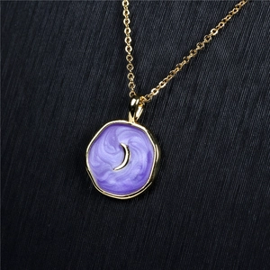 Macro view of gold crescent moon pendant with purple enamel detail on a delicate chain