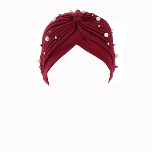 Close-up of red pleated turban featuring white pearls and silver beaded ornaments