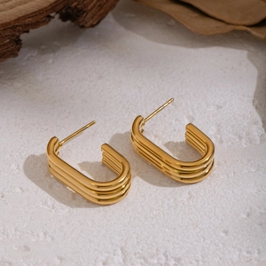 Macro view of gold-plated multi-layer C-shaped earrings on natural stone background