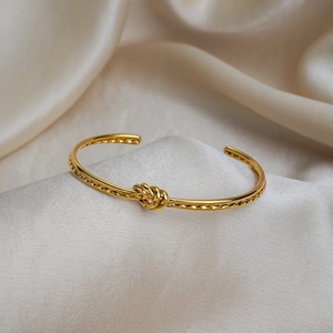 Détail d'un bracelet jonc noué en or posé sur un tissu de soie champagne luxueux