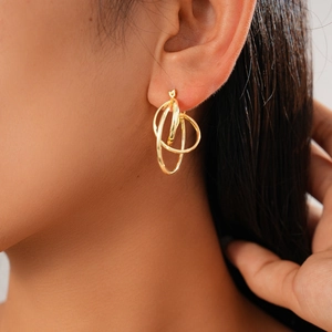 Close-up of gold geometric interlocking hoop earrings worn by a model in a minimal style