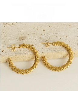 Detail of 18K gold plated stainless steel twisted rope hoop earrings on stone background