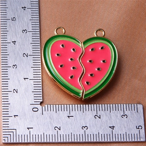 Macro shot of watermelon heart charms showing dimensions with a metal ruler measurement