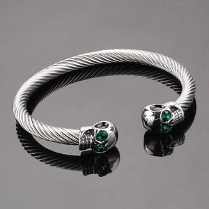 Gothic silver twisted cable cuff bracelet featuring skull heads with green crystal eyes