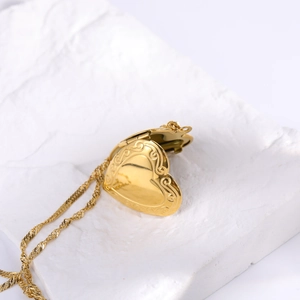 Golden heart locket necklace with embossed floral patterns on white textured stone