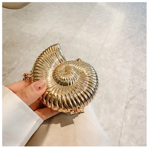 Macro detail of golden conch-shaped metal shell clutch bag with delicate spiral texture