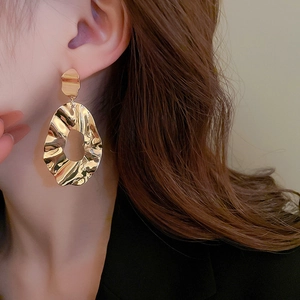Macro detail of gold irregular geometric earrings with hammered metal texture on model