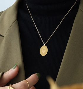 Close-up of gold oval flower pendant necklace on olive blazer and black turtleneck