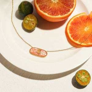 Detail of gold ocean style necklace with pink shell inlay and shell charm on white plate