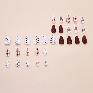 Press on nails with caramel plaid, black polka dots, and bow designs in almond shape