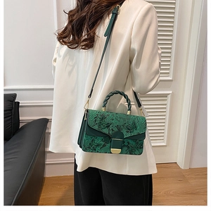 Sac brodé floral vert foncé avec fermoir doré porté sur une veste de costume blanche