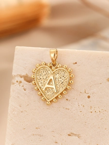 Macro detail of gold heart pendant with letter A engraving and hammered texture finish