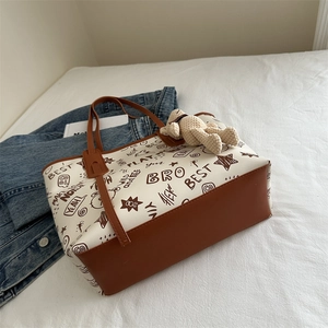 Brown and white tote bag with graffiti prints and a knit bear charm on white bedding