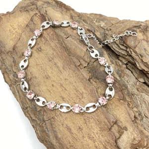 Close-up of silver-tone chain bracelet with pink rhinestones on a natural rock background