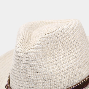 Close-up of cream woven straw fedora hat featuring a brown ribbon with decorative stitching