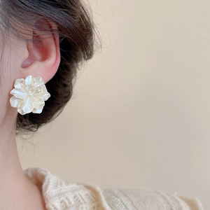 Dettaglio di orecchini a fiore con perle e petali bianchi stratificati indossati da modella