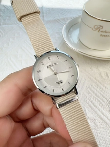 Close-up of minimalist quartz watch with beige nylon strap and silver metal case