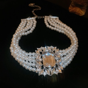 Macro detail of layered pearl necklace with square crystal pendant on black background