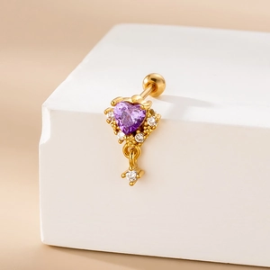Detail of a golden heart piercing with a purple zircon and small crystals on a white cube