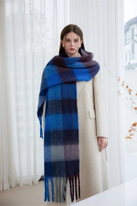 Detailed view of thick blue purple and grey plaid scarf with fringes on beige coat