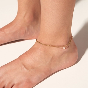 Double-layered gold stainless steel anklet with a shell pearl on a model's ankle