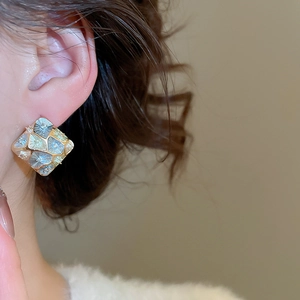 Close-up of geometric square stud earrings with vintage multi-tone textured metal finish
