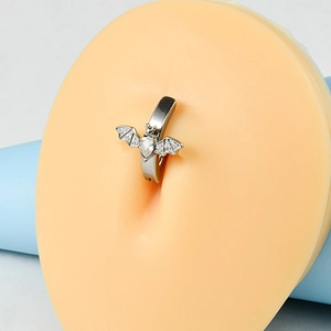 Detail of silver bat navel ring with heart zirconia on a silicone belly model