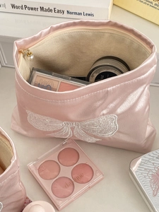 Macro view of pink satin cosmetic bag with white bow embroidery and pearl zipper detail