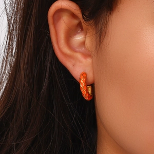 Fashionable orange enamel hoop earrings with gold quilted pattern on a female model