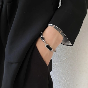 Close-up of a silver chain bracelet with a black rectangular stone on a male wrist