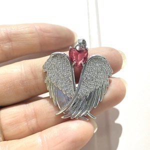 Macro shot of silver angel wing pendant with small diamonds and a red heart gemstone
