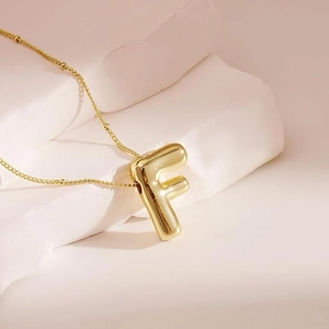 Close-up of golden balloon-style 3D letter F pendant with beaded chain necklace