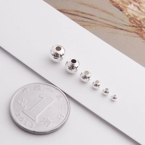 Macro shot of 925 silver round beads in various sizes next to a coin for scale