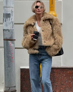 Street style shot of a khaki faux fur jacket paired with blue straight jeans and coffee