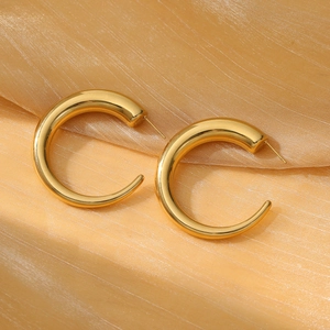 Detail of chunky gold C-shaped titanium steel earrings on shimmering textured fabric