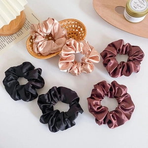 Close-up of six satin scrunchies in black, champagne gold and burgundy on a white table