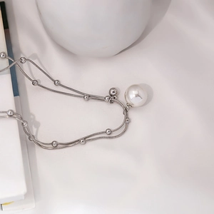 Detail of layered silver snake chain with round white pearl on white silk fabric
