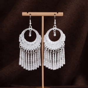 Dettaglio degli orecchini etnici in argento con nappine e motivi tribali incisi