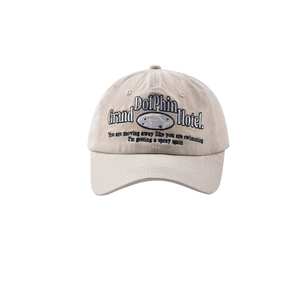 Detailed close-up of beige baseball cap featuring green dolphin and letter embroidery
