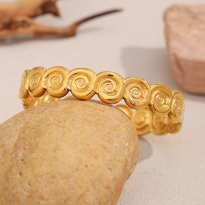Detailed view of an 18K gold plated conch spiral patterned bangle on a textured stone