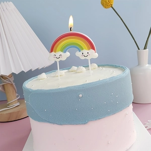 Rainbow cake candle with smiling clouds and flickering flame on pink surface