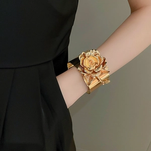 Detailed view of wide gold metal cuff bracelet featuring a large 3D rose flower design