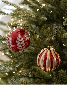 Gros plan de boules de Noël rouges et dorées avec motifs de feuilles sur une branche de sapin